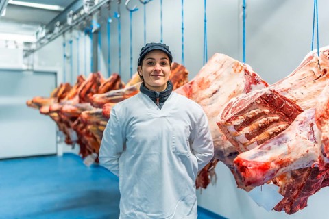 Three quarter length frontal portrait of a proud and happy woman butcher in a meat processing