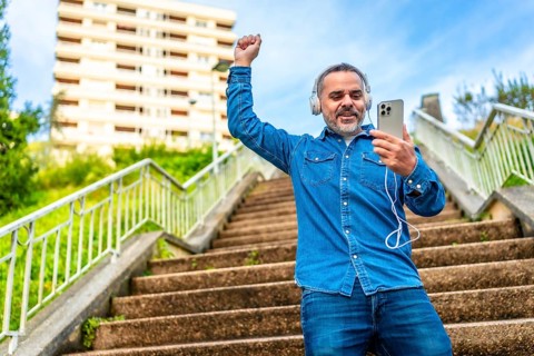 Mature man dancing while listening to music with phone in an urban stairs in the city