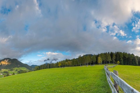 View along a wooden fence across a pasture to the mountains in the evening light, Dolomites, Odle