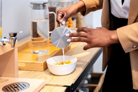 Businesswoman pouring milk into a bowl of cereal, enjoying breakfast during a business trip