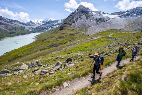 Three mountaineers on a hiking trail at a blue mountain lake, reservoir Lac des Dix, behind