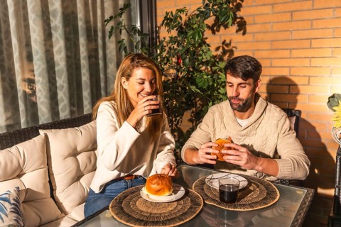 Smiling man and woman enjoying burgers and beverages on a cozy terrace, creating a warm and
