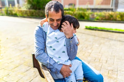 Grandfather hugging grandson while sitting on a park bench, enjoying a tender moment together