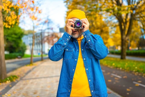 Frontal portrait of a mature modern man photographing in the city while visiting it in autumn