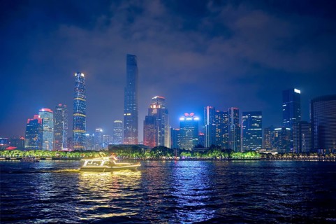 Guangzhou cityscape skyline over the Pearl River with tourist boat illuminated in the evening.