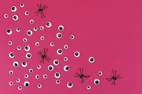Halloween flat lay with lots of spooky googly eyes and plastic spiders on pink background with