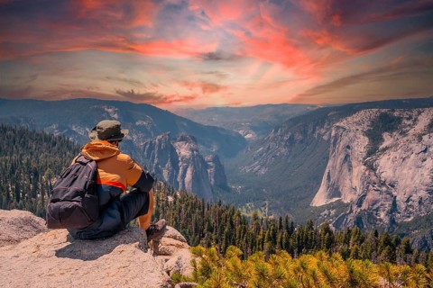 A young man on the trek sitting on the Sentinel Dome lookout in Yosemite National Park looking at