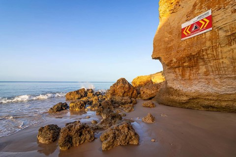 ROCKFALL UNSTABLE CLIFFS, KEEP A SAFE DISTANCE is written in English on a warning sign in Portugal