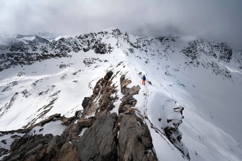 Mountaineer descending the narrow ridge of Piz Laviner, view of mountain panorama in wintry