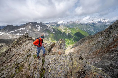 Mountaineer on a steep rocky ridge, at the summit of Lasörling, view of mountains of the Venediger