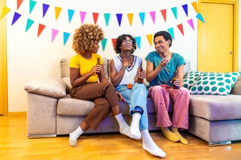Multi-ethnic friends chatting during party at home sitting on the sofa with beers and karaoke