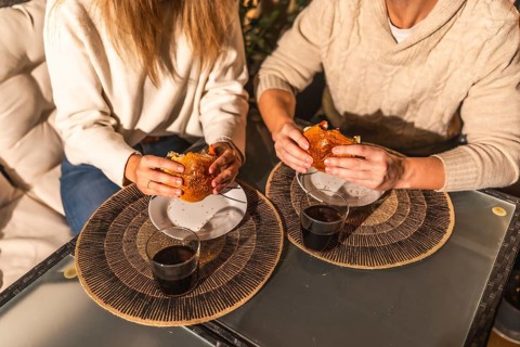 Couple sharing a moment eating burgers and drinking, probably wine or soda, sitting at a table with