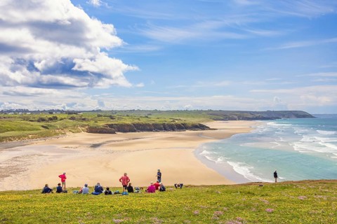 Group of hikers resting on a meadow with a scenics view at a sand beach with breaking waves and a