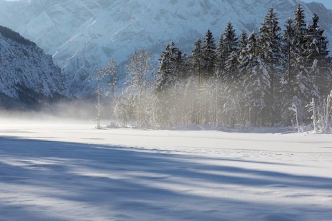 Misty morning on Lake Almsee which is frozen and snow covered. Snow on the forest with blue sky