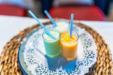 Three vibrant smoothies in glass cups with straws, placed on a decorative table setting, adding a