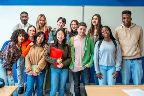 Multi ethnic group of university students standing together in a classroom, sharing smiles and