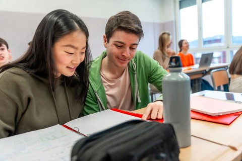 Two high school students are working together on a project in a classroom, demonstrating teamwork