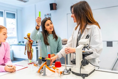 Female teacher assisting students during a chemistry experiment in a school laboratory, promoting