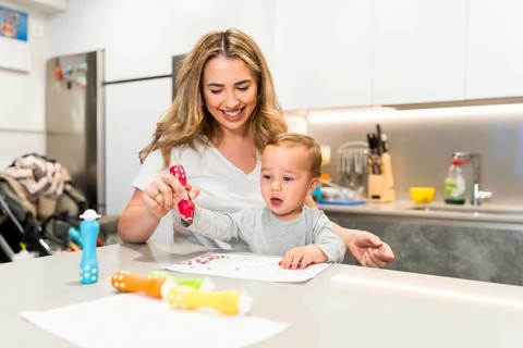 Smiling mother and baby boy having fun drawing together with colorful dot markers in a modern