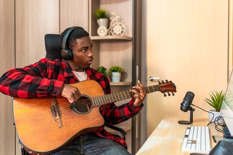 Concentrated young man playing the acoustic guitar in his home studio, composing a new song and