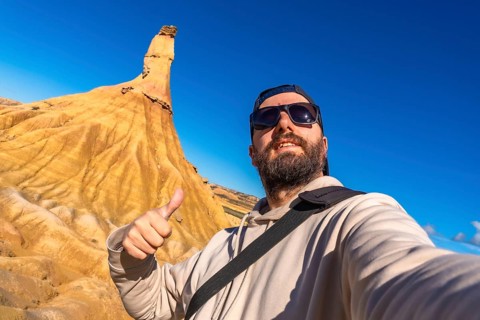 Tourist taking a selfie and gesturing thumbs up in front of a sandstone peak in bardenas reales