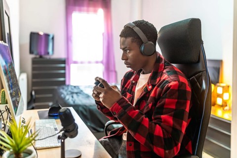 Young man concentrating on playing video games, using headphones and a controller, in his bedroom