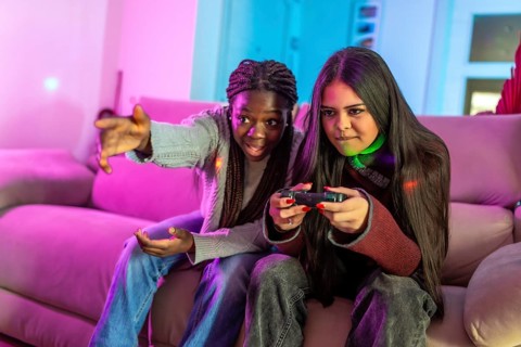 Two focused female students enjoying a gaming session on a cozy sofa at home, sharing laughter and