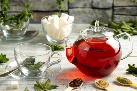 Touched teapot, glasses with mint, pieces of sugar and different types of tea on a table in front