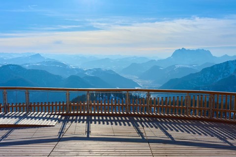 Wooden platform with a view of snow-covered mountains under a blue sky, Steinplatte, Waidring,