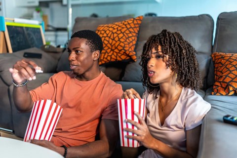 Relaxed couple enjoying a movie night at home, sitting on the floor in front of their sofa and
