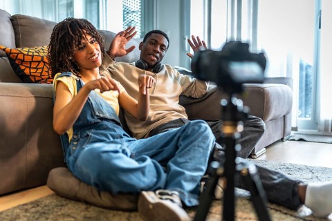 Two influencers recording a lively vlog in their cozy living room, gesturing enthusiastically and