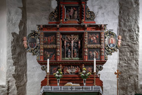 Richly decorated wooden altar in front of a stone wall, adorned with images of saints, candles and