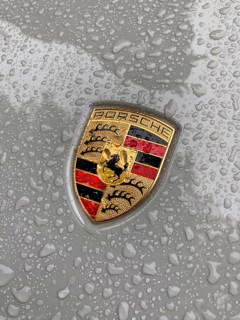 Porsche crest on grey bonnet of sports car with sparkling raindrops, international