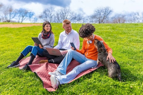 Three young coworkers are taking a break from work outdoors, using laptop, tablet and smartphone,