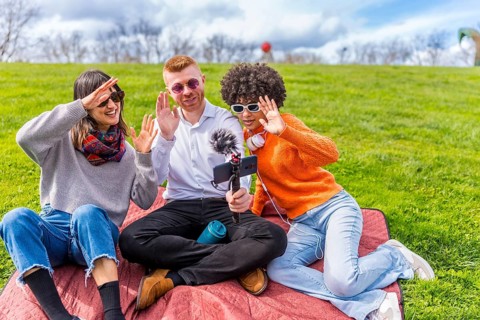 Three content creators waving cheerfully at the camera while filming a video blog outdoors in a