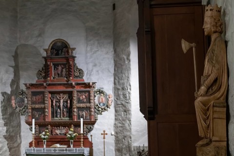 Richly decorated wooden altar in front of a stone wall, decorated with images of saints, wooden