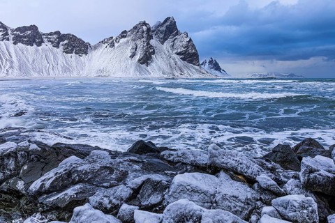 Iced rocks on the beach of Stokkness, behind them the snowy rocky slopes of Vestrahorn, near Höfn,