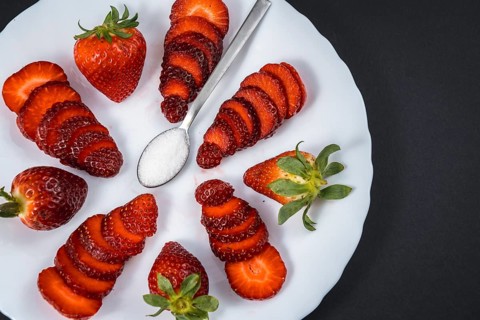 Natural strawberries on a white plate with a spoon of sugar with black background