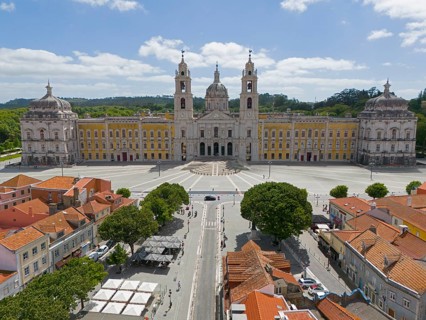 Historic baroque-style palace with yellow façade and two towers, under blue sky and large square,