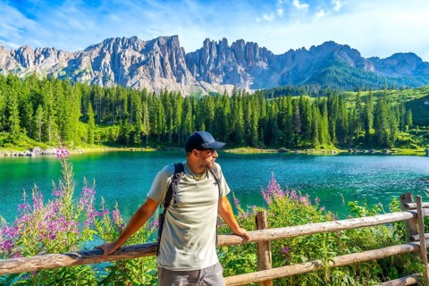 Hiker admiring the stunning landscape of lake carezza with the latemar mountain range in the