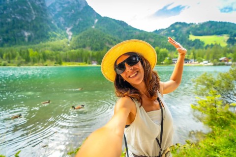 Happy tourist taking a selfie at lake dobbiaco with ducks swimming in the emerald green water and