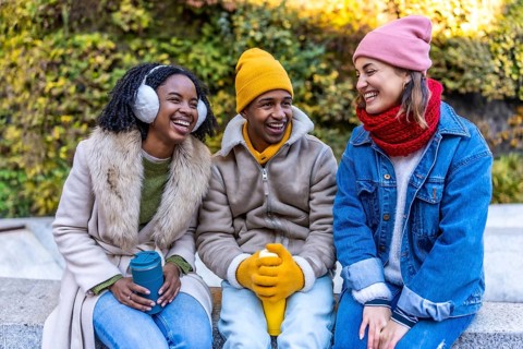 Three cheerful young multi ethnic friends sitting outdoors in the city on a cold winter day,