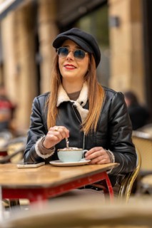 Young woman wearing sunglasses and hat stirring cappuccino at a parisian outdoor cafe, enjoying a