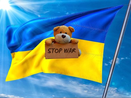 Symbolic picture, Ukraine flag in front of a bright sky, sad little bear with Stop War sign, Donald