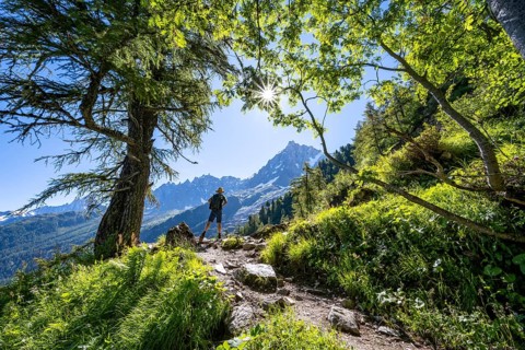 Hiker on hiking trail with sun star, hiking trail La Jonction, behind summit of Aiguille du Midi,