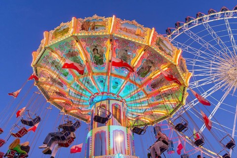 Illuminated carousel and Ferris wheel at night in a lively amusement park, funfair, wave flight,