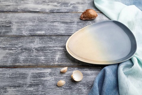 Empty blue ceramic plate on gray wooden background and blue textile. Side view, copy space