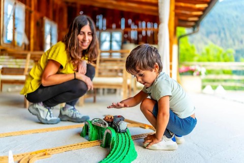 Young boy enjoying a toy train set on a sunny patio with an adult nearby