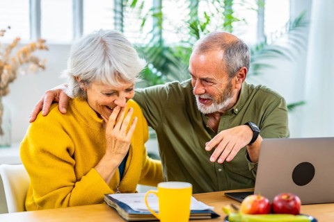 Senior woman looking at household finances notes and expressing surprise and happiness while her