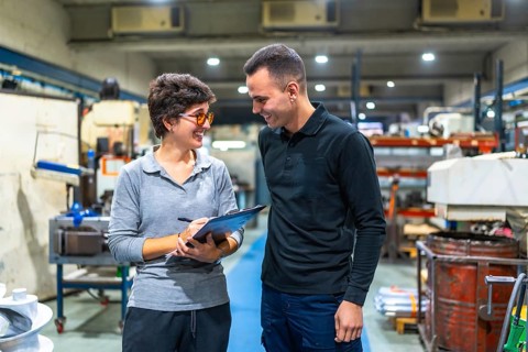 Male worker talking happily to a female workshop manager while writing on clipboard